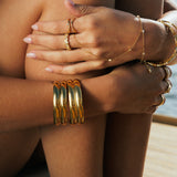 Close-up of a person's arm with gold jewelry by a body of water. Gold cuff bracelets.