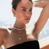 Woman wearing gold jewelry and a black strapless top with a blurred background