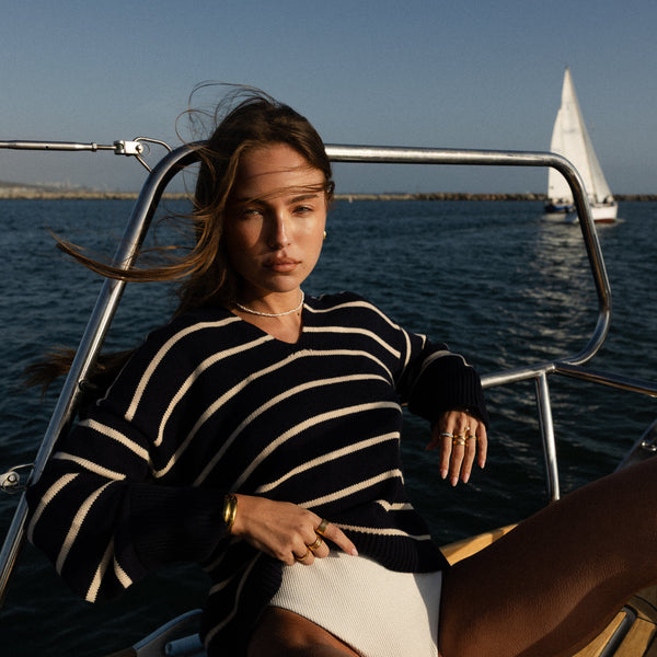 Woman sitting on a boat with another sailboat in the distance wearing waterproof jewelry and pearl necklace and gold rings