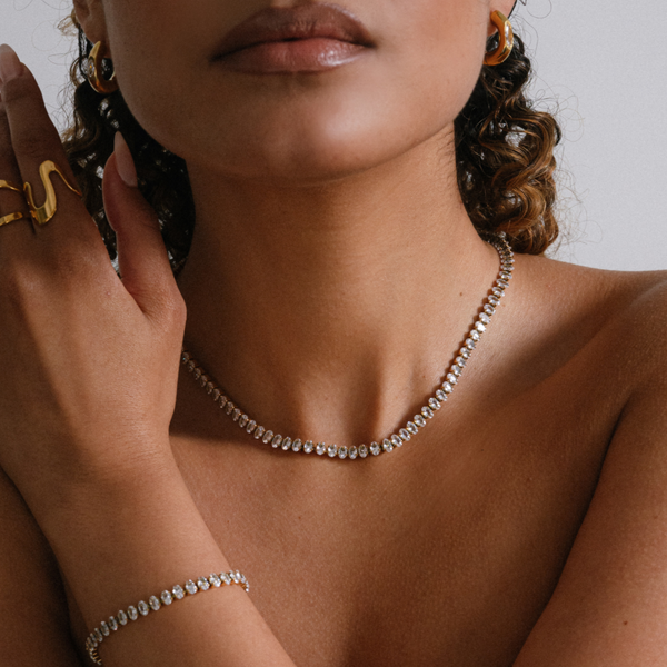 Woman wearing a necklace, bracelet, and ring with a neutral background